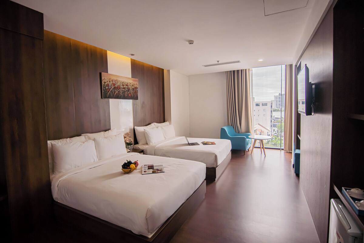 A hotel room with two beds, a TV, a desk, and a view of the city.