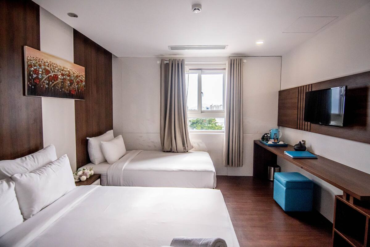 A hotel room with two beds, a desk, a TV, and a window with curtains.
