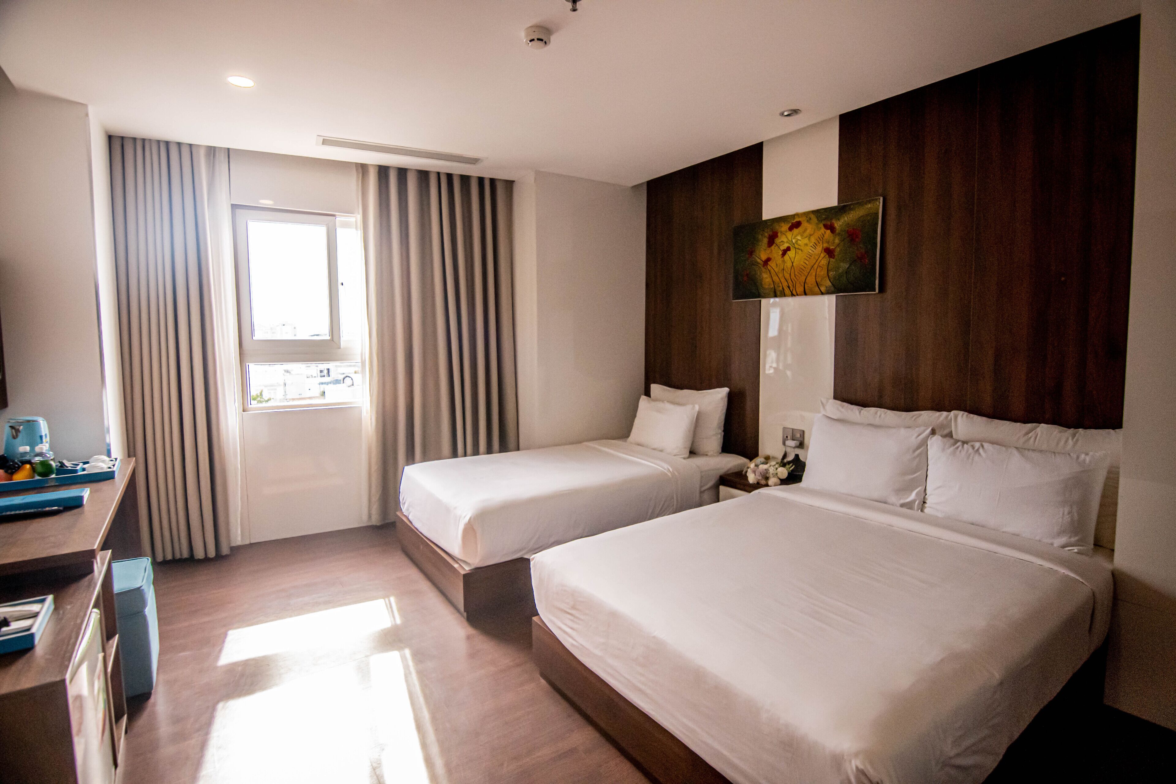 A hotel room with two beds, a desk, and a window with curtains.