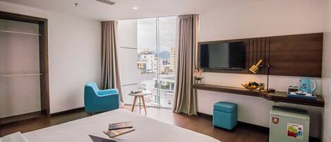 A hotel room with a bed, a desk with a laptop, a TV, and a view of the city.