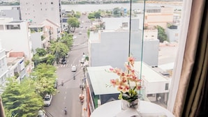 A room with a view of a cityscape, a small table with a vase of flowers, and two blue chairs. - Gold Central Hotel by Haviland (Da Nang)