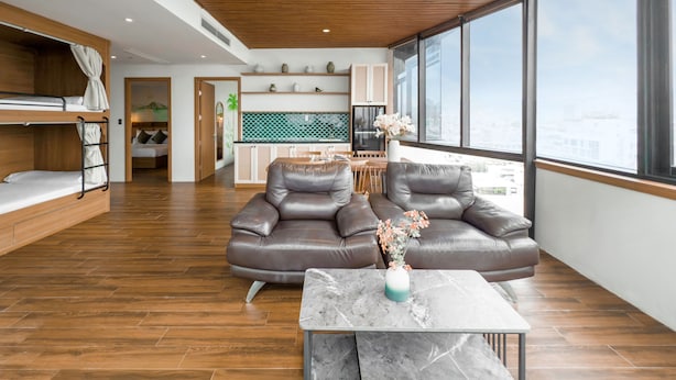A modern living room with a wooden ceiling, a sofa, a coffee table, and a view of the city through large windows. - Gold Central Hotel by Haviland (Da Nang)