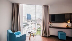 A modern room with a large window, a flat-screen TV, a small table, and a blue chair. - Gold Central Hotel by Haviland (Da Nang)