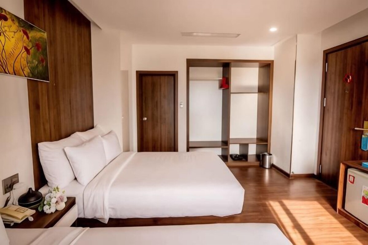 A hotel room with a large bed, a bedside table with a phone and flowers, a wardrobe, and a door leading to a bathroom.