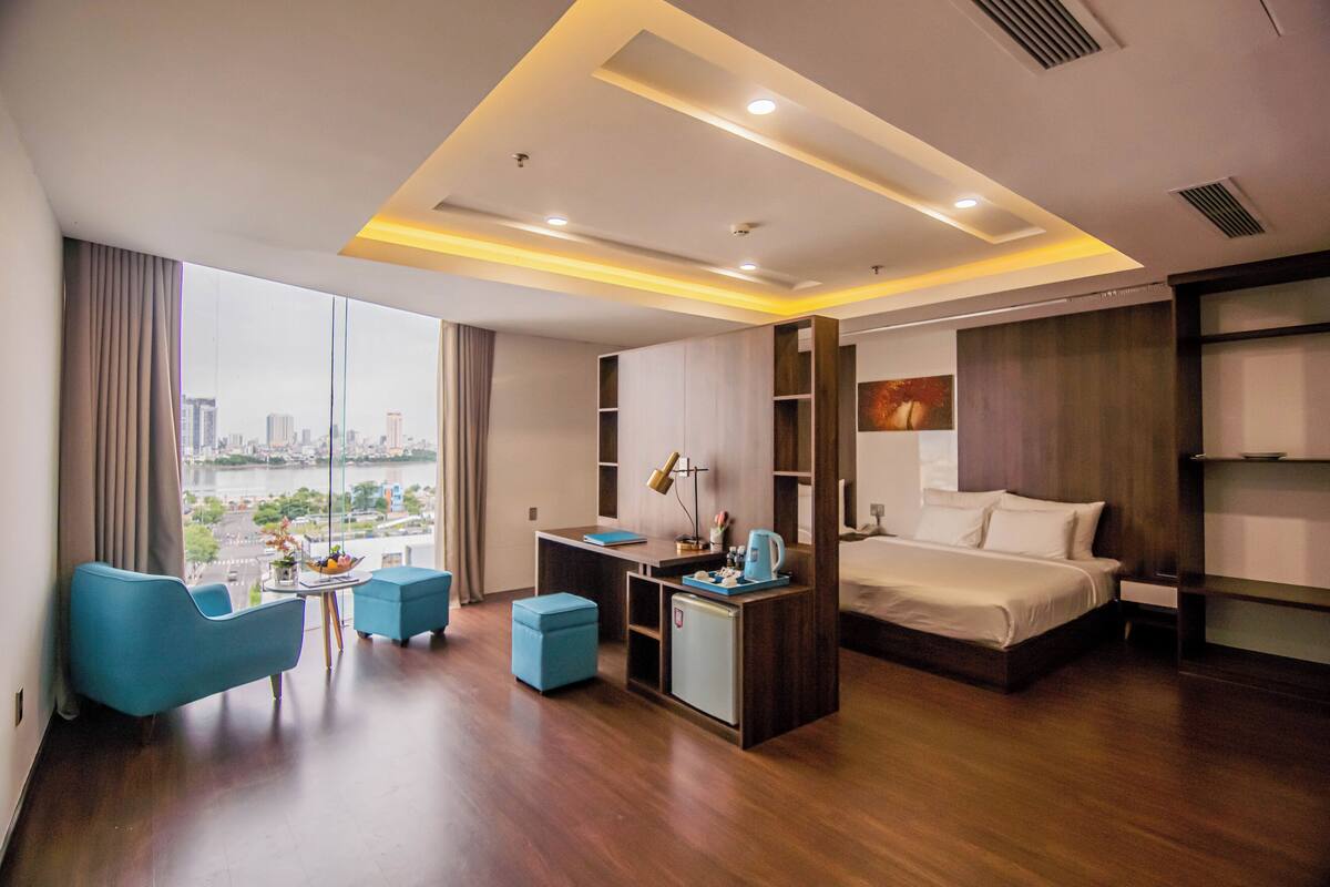 A modern hotel room with a large bed, a desk, a chair, and a view of the city.