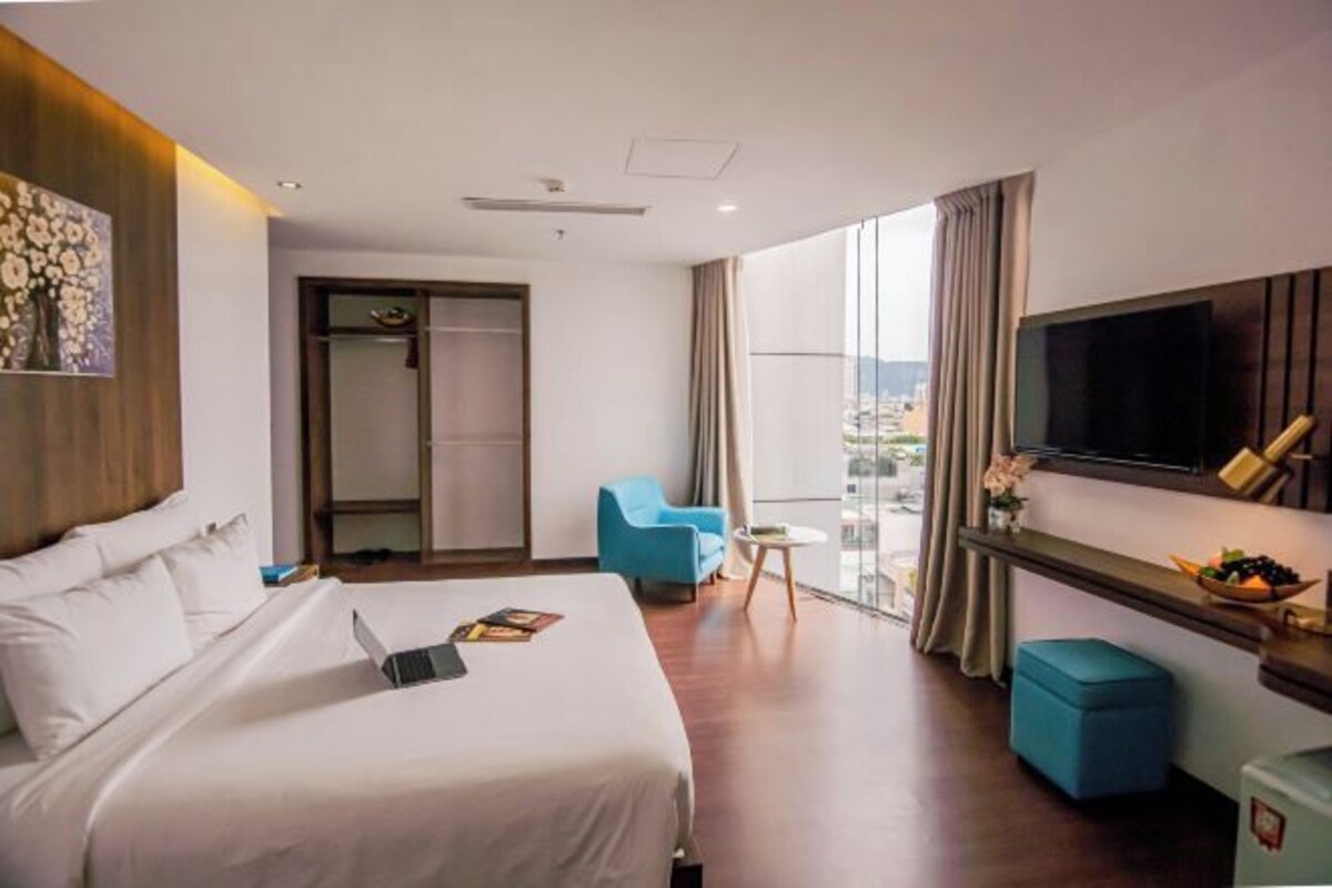 A hotel room with a bed, a TV, a small table, a chair, and a window with a view.