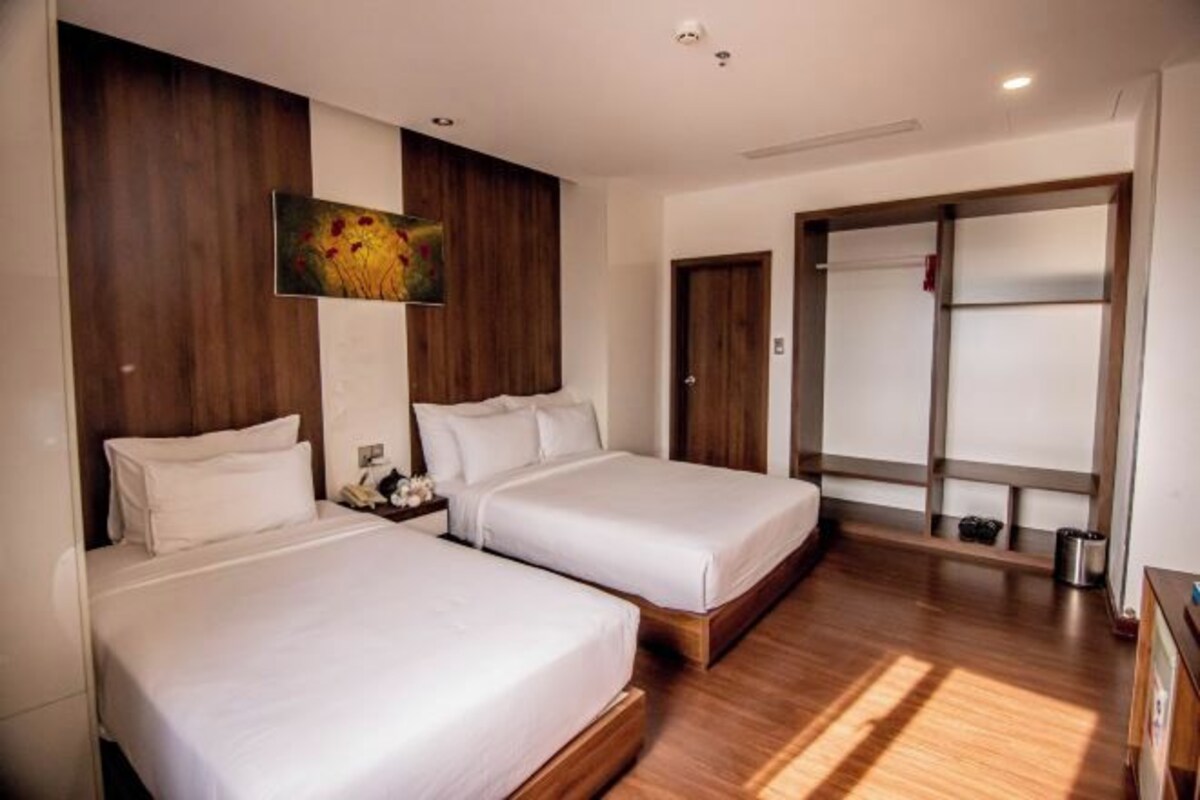A hotel room with two beds, wooden flooring, a large mirror, and a painting on the wall.