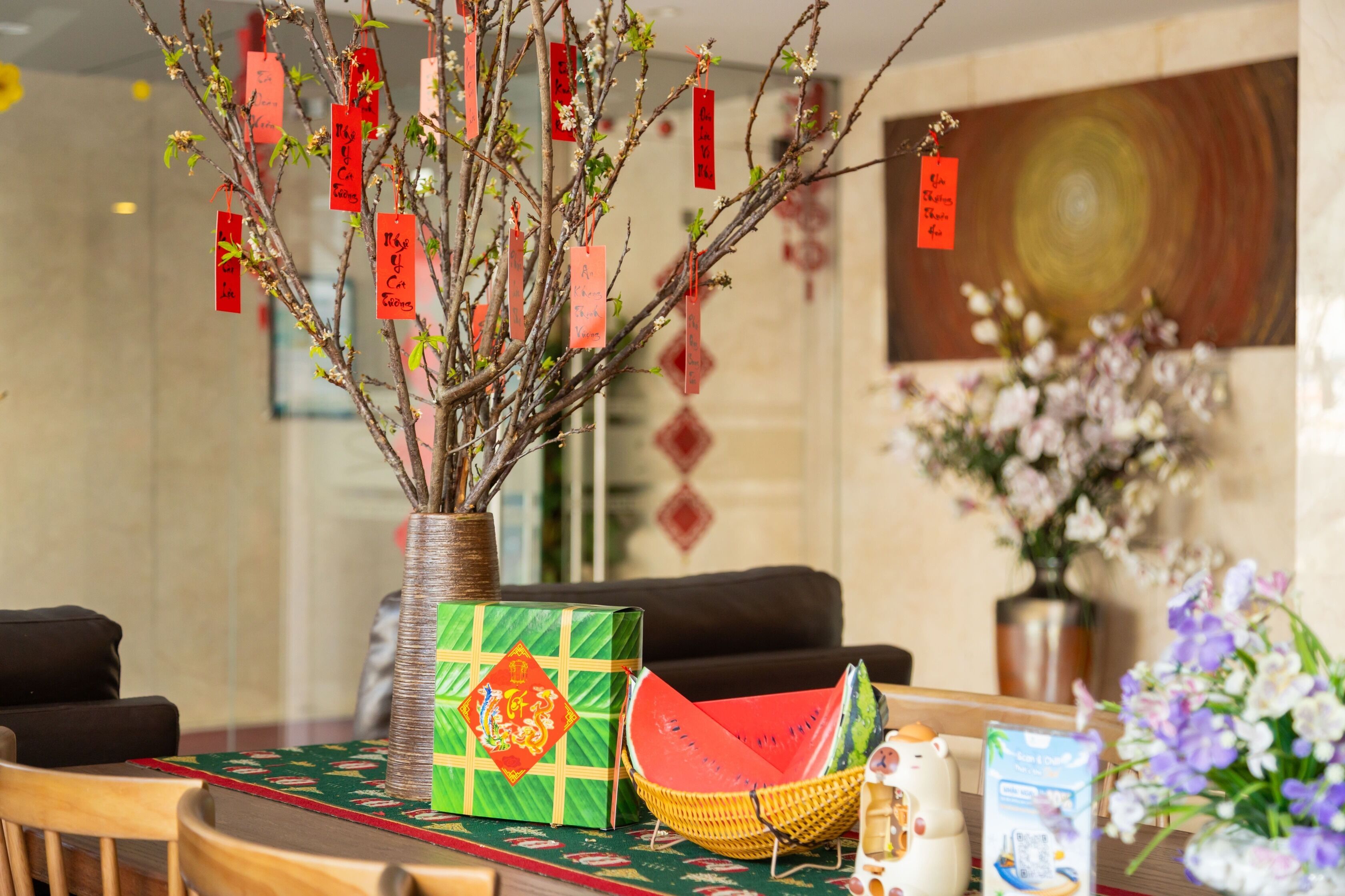A table with a vase of branches, a green gift box, a woven basket, and a decorative item.