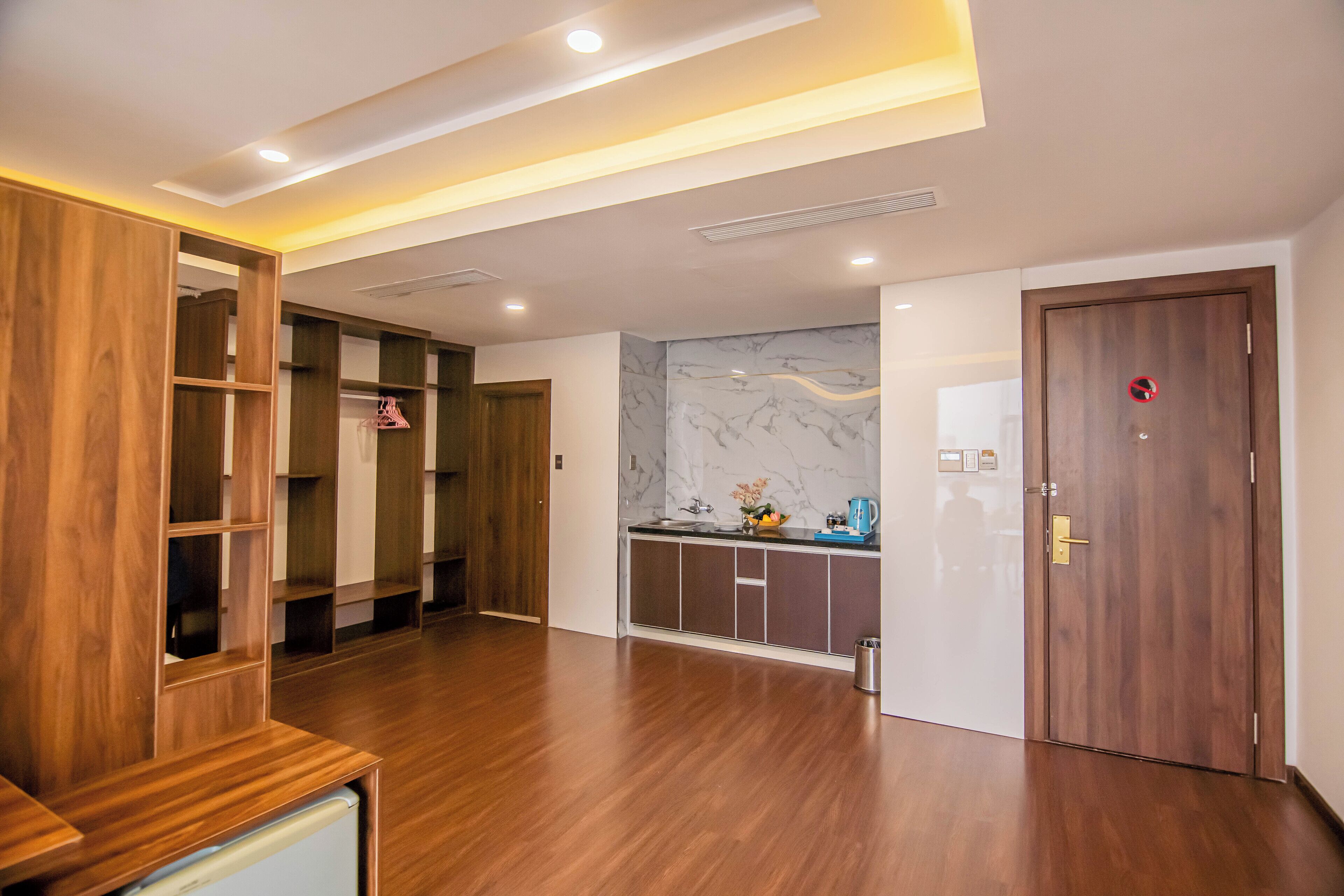 A modern hotel room with wooden flooring, built-in wardrobes, a marble backsplash, and a wooden door with a red circle sign.