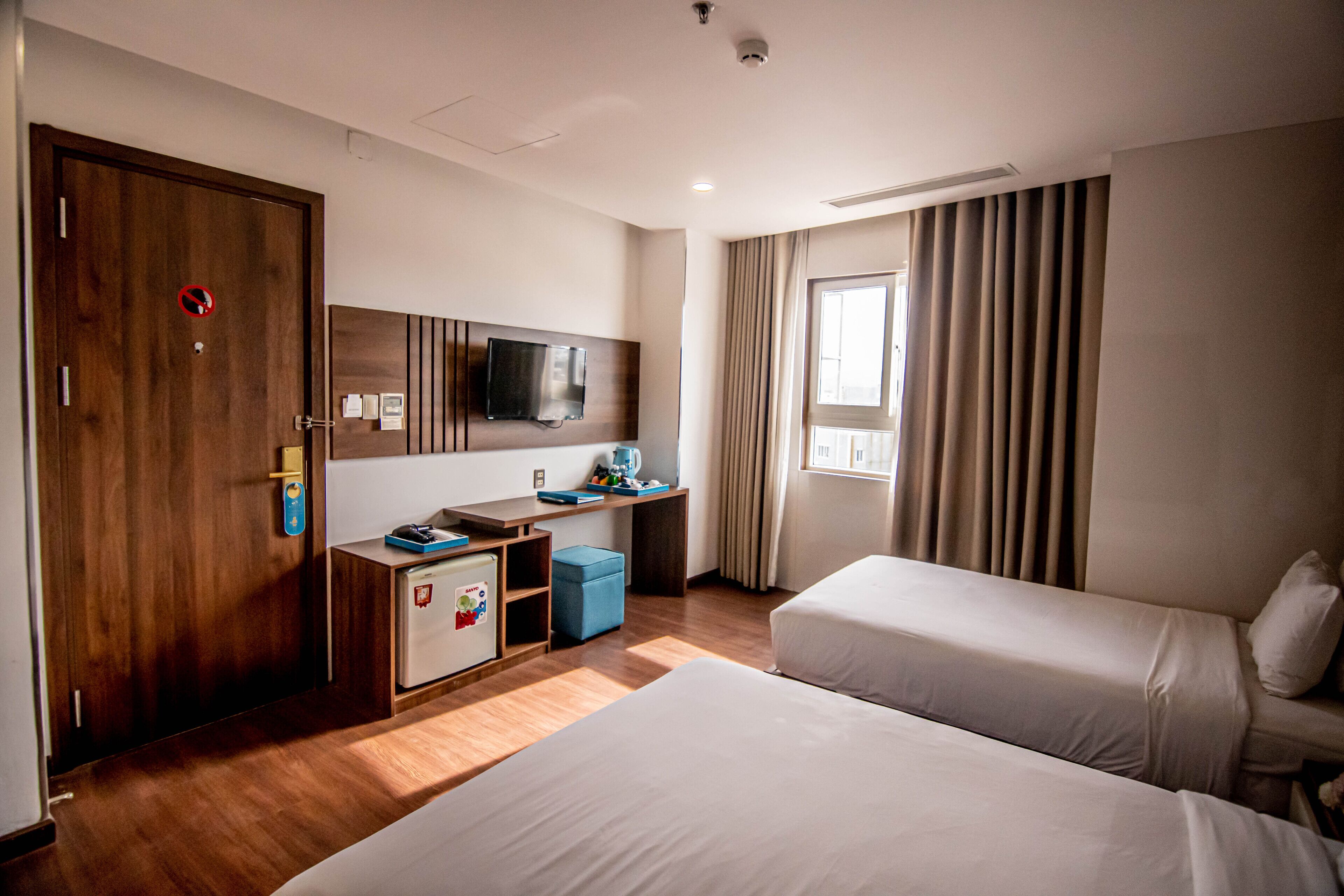 A hotel room with two beds, a desk, a TV, and a window with curtains.