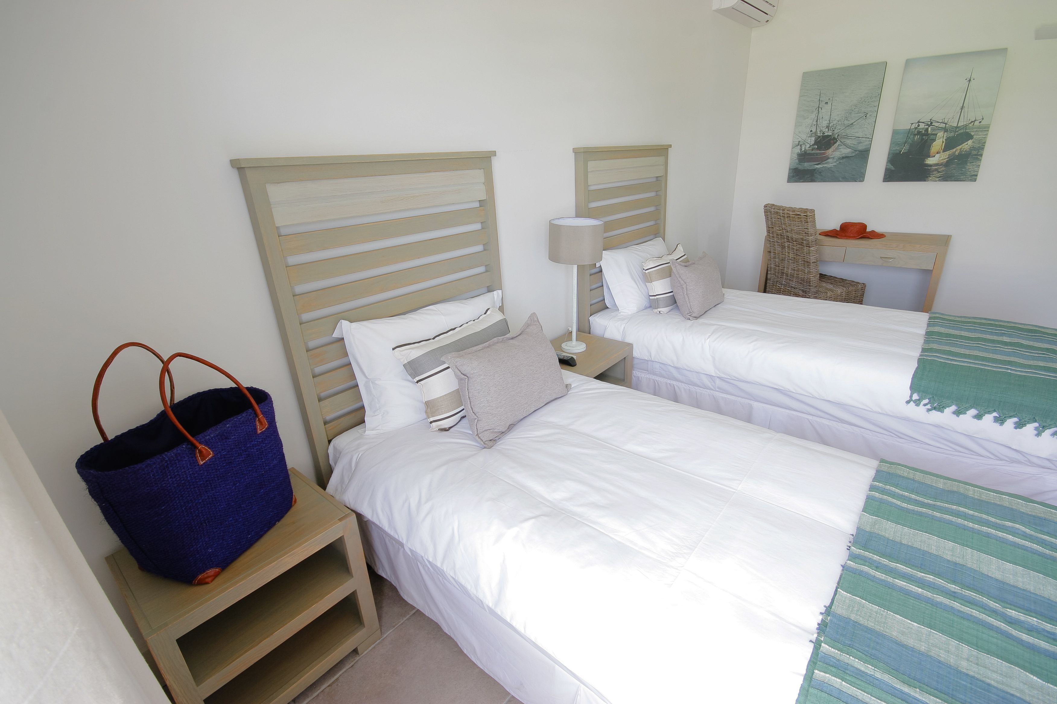 A double room with two beds, a desk, a chair, and a large blue bag on a nightstand.
