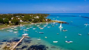 Vista aérea de uma área costeira com inúmeros barcos atracados em uma marina, cercada por vegetação exuberante e mar azul cristalino.
