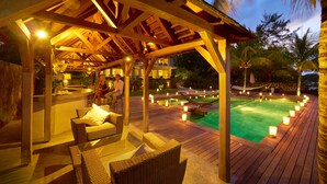 Um deck de madeira com área de estar externa e piscina ao entardecer.