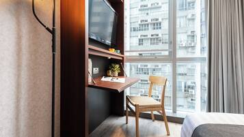 Una habitación de hotel con un ventanal grande, un escritorio con televisor de pantalla plana, una silla y una cama.