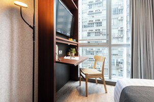 Una habitación de hotel con un ventanal grande, un escritorio con televisor de pantalla plana, una silla y una cama.