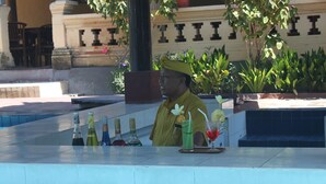 A bar area with a tiled counter, bottles of beverages, and a barista in a uniform. - Bakung Beach Resort (Kuta)