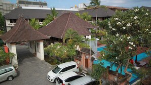 A residential area with traditional architecture, including a house with a tiled roof and a small pavilion. There is a swimming pool with a blue cover, surrounded by greenery and flowering plants. - Bakung Beach Resort (Kuta)