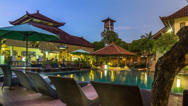 A pool area with lounge chairs and umbrellas, a traditional building with a tiled roof, and a tower structure in the background. - Bakung Beach Resort (Kuta)