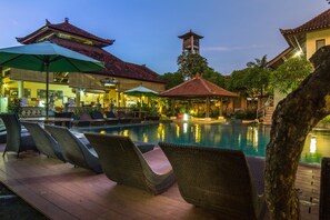 A pool area with lounge chairs and umbrellas, a traditional building with a tiled roof, and a tower structure in the background. - Bakung Beach Resort (Kuta)