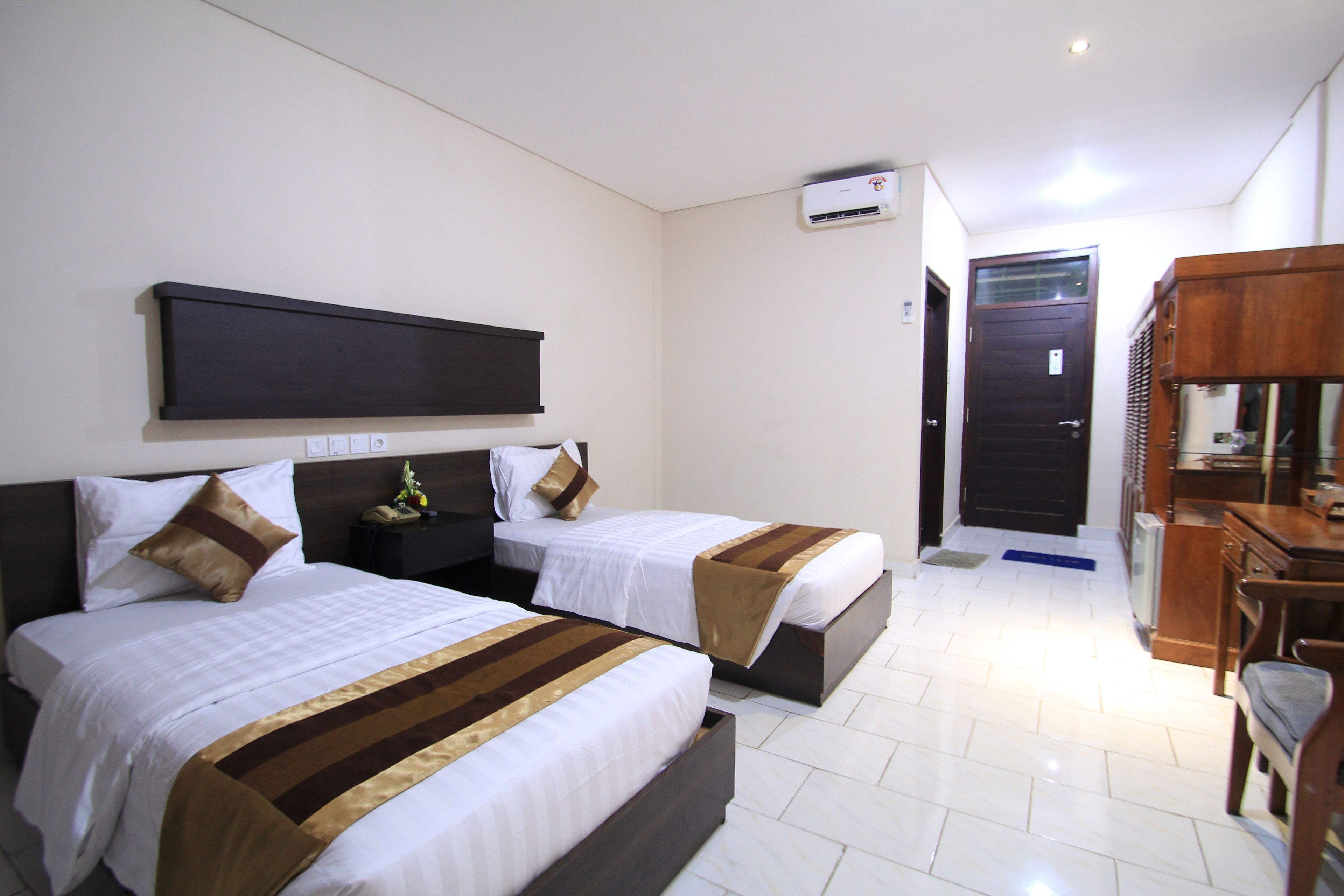 Habitación de hotel con dos camas, un televisor de pantalla plana montado en la pared, un escritorio con una silla y un armario de madera.