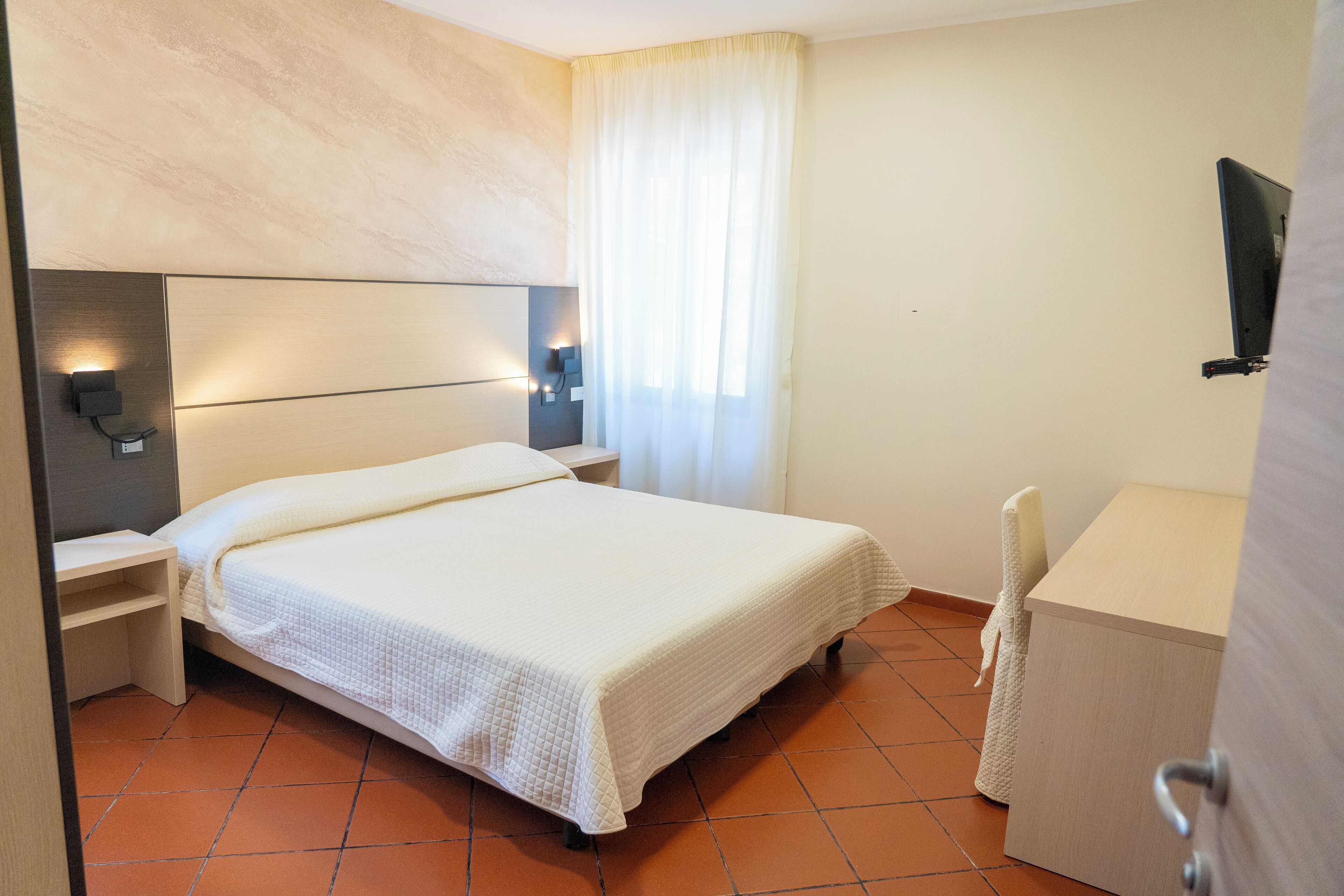 Hotellihuone, jossa on sänky, yöpöydät, työpöytä ja tuoli.