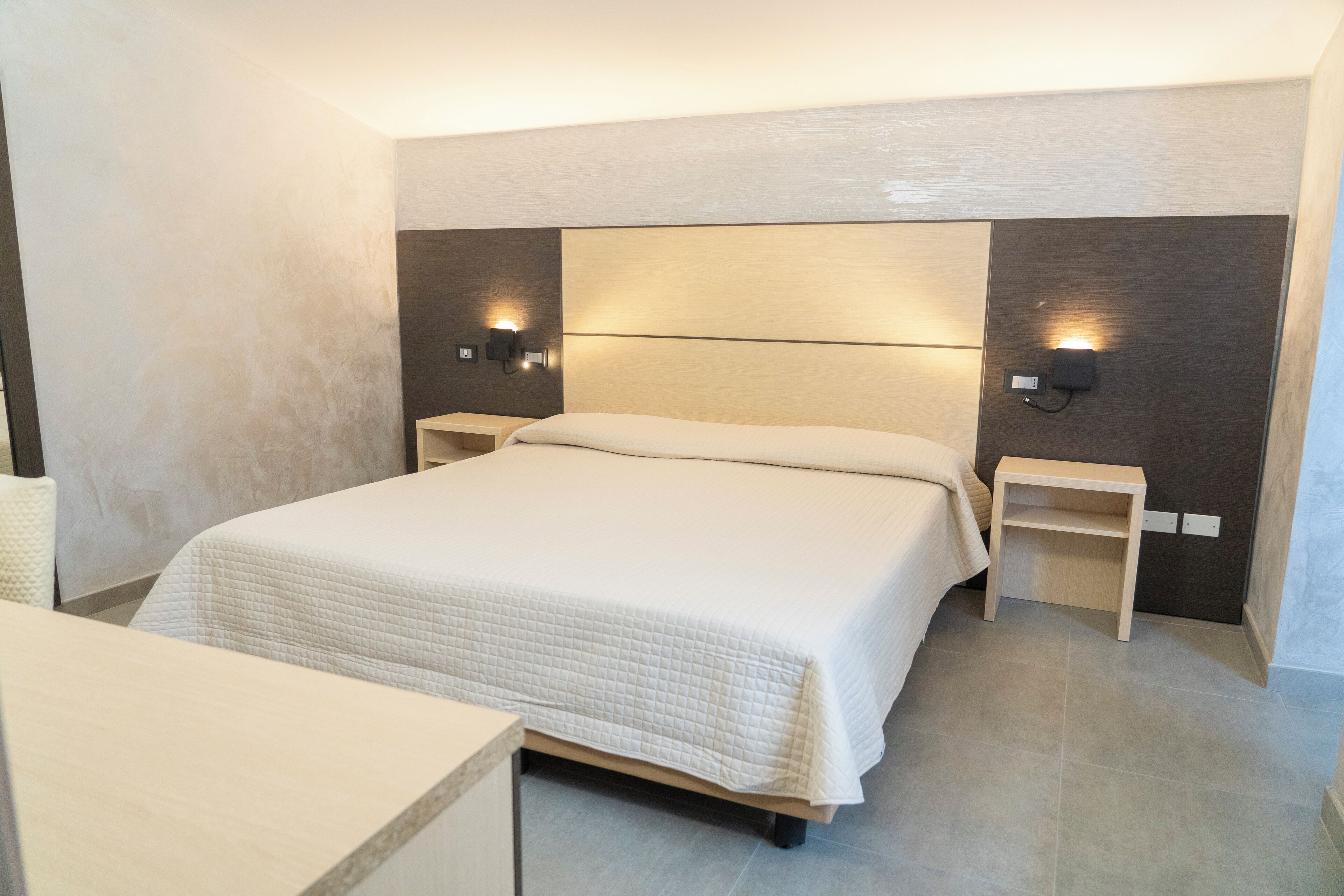 Una habitación de hotel moderna con una cama grande, mesitas de noche e iluminación empotrada.