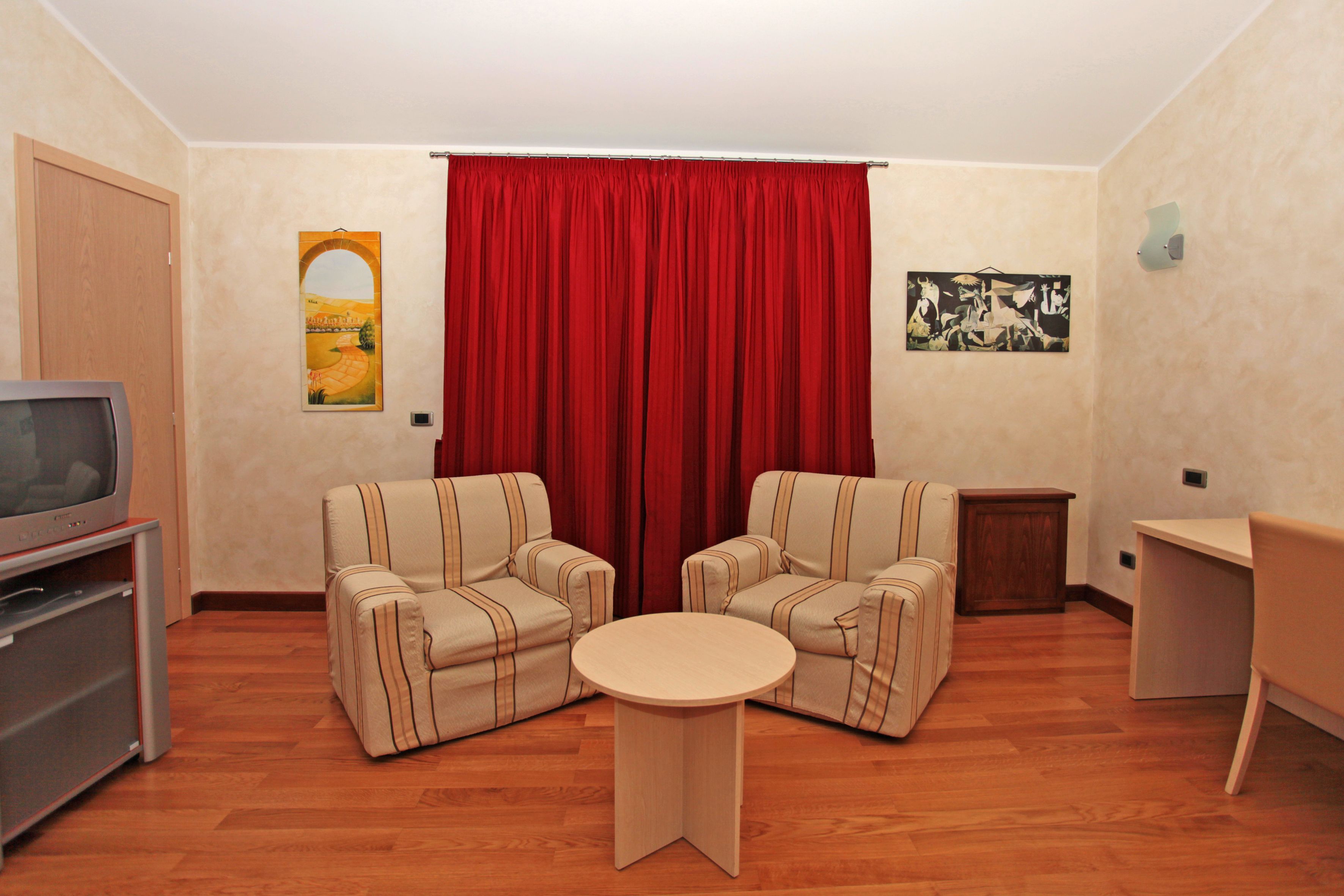 A living room with two armchairs, a small round table, a television, and a red curtain.