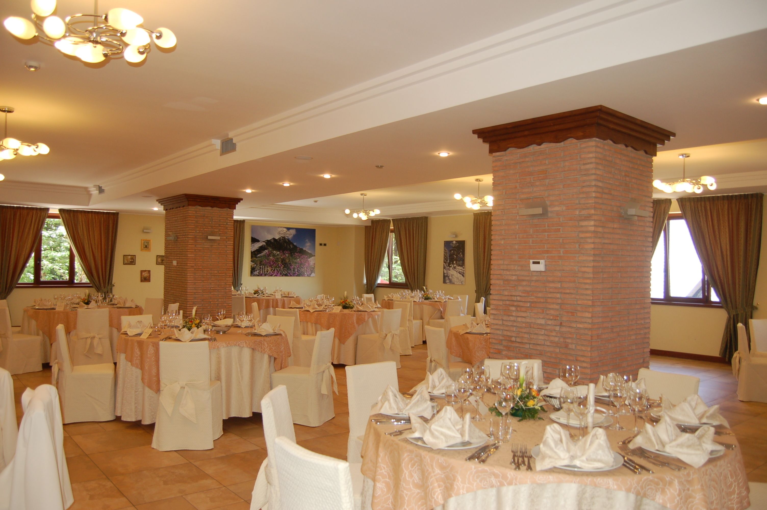 A banquet hall with round tables set for dining, featuring white chairs and tablecloths.