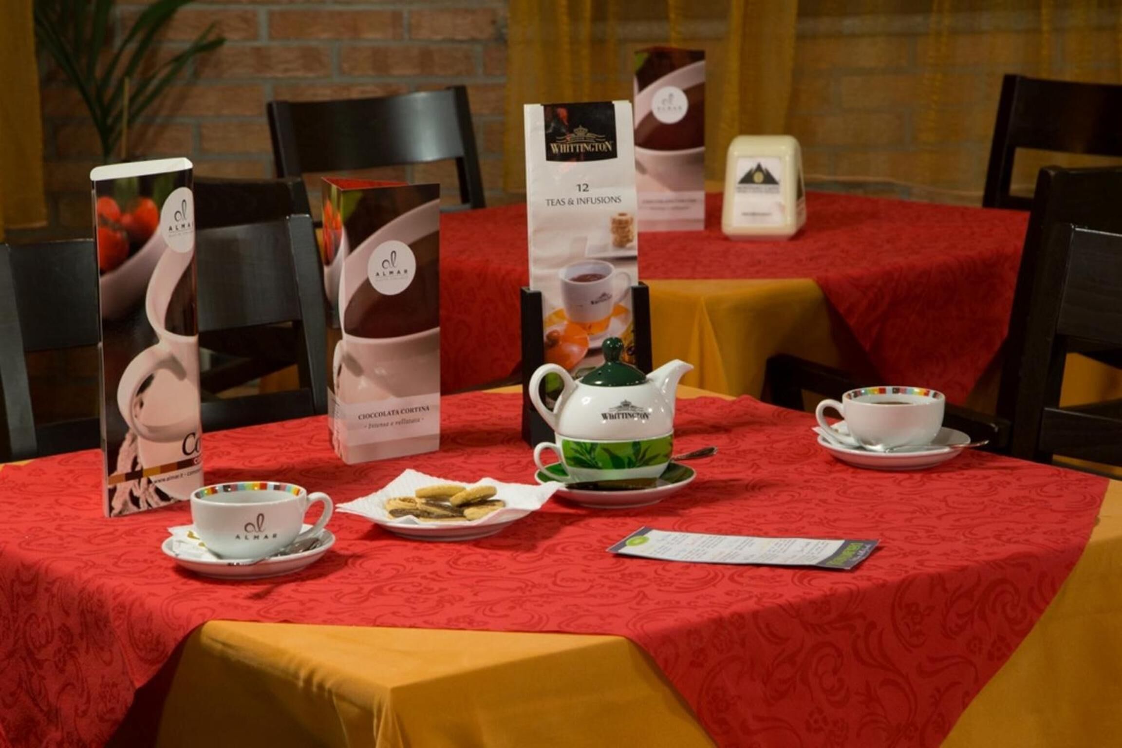 A table set for a tea service with a red tablecloth, a teapot, cups, and a menu stand.