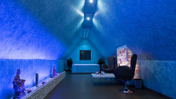 A spa room with a blue-lit ceiling, a massage chair, a small table with a bottle, and a window. - Albergo della Posta (Taverna)