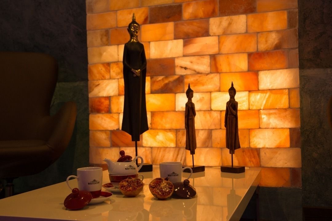 A table with a teapot, cups, and a decorative Buddha statue against a textured wall.