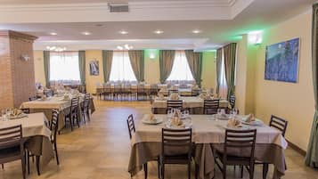 Comedor con varias mesas dispuestas para una comida, con pared de ladrillo y un ventanal con cortinas.