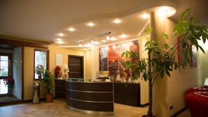 A reception area with a curved desk, potted plants, and a red leather couch. - Albergo della Posta (Taverna)