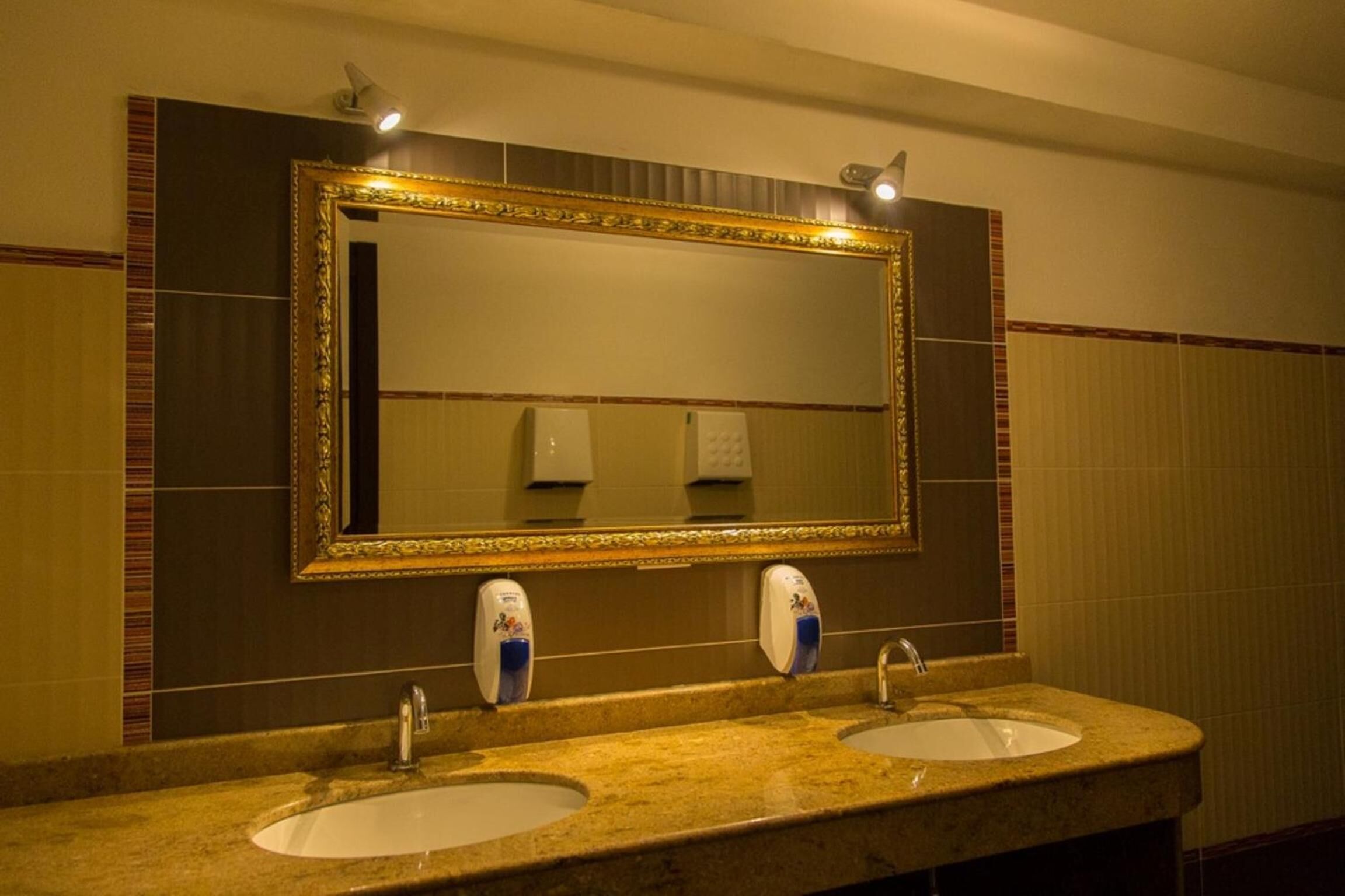 A bathroom with two sinks, a large mirror, and hand sanitizer dispensers.