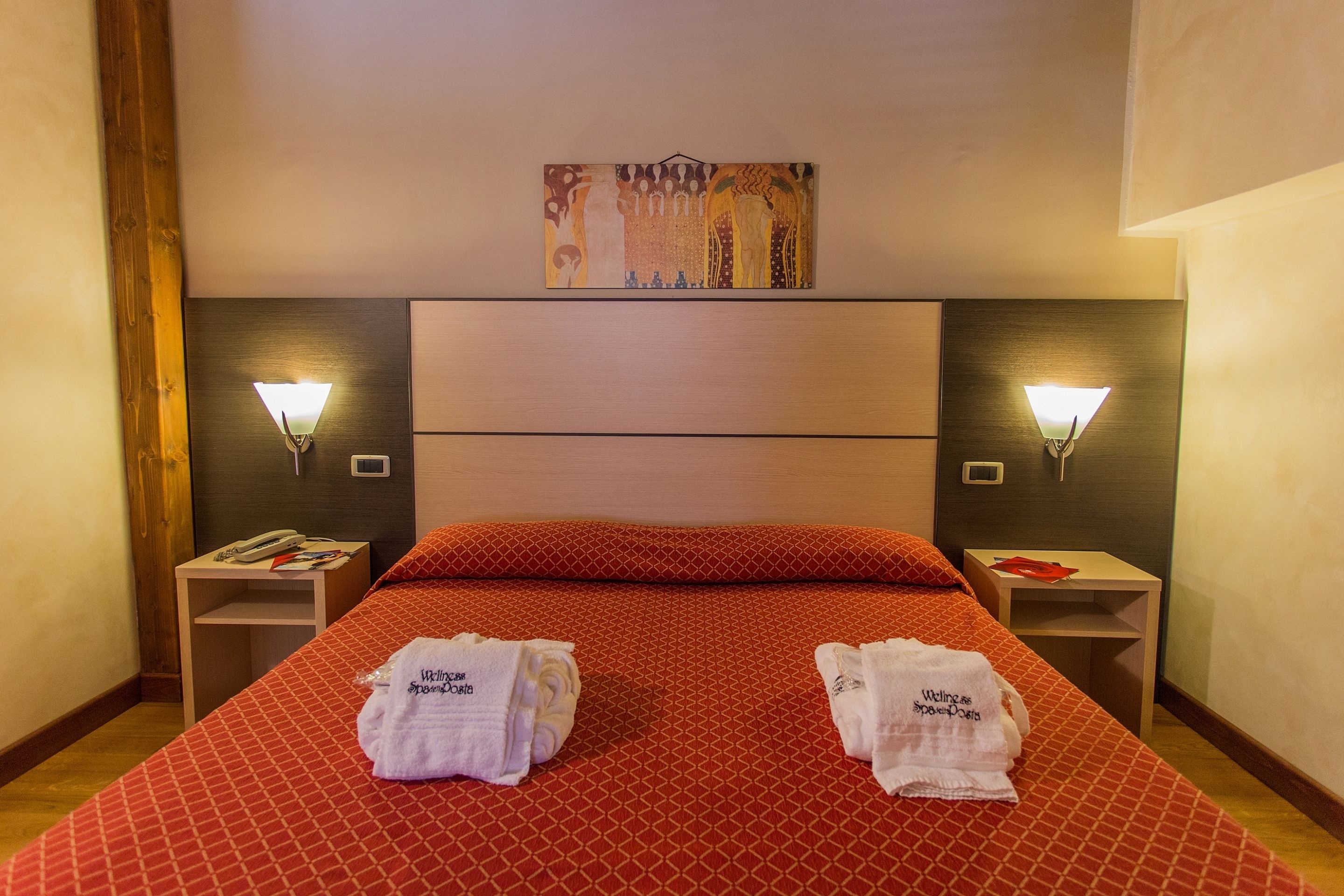 Une chambre d’hôtel avec un grand lit, deux tables de chevet, un tableau au-dessus du lit et deux serviettes sur le lit.