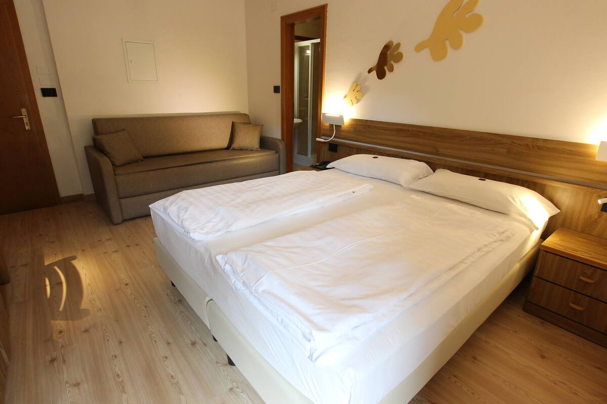 Un dormitorio con una cama grande, cabecera de madera, mesita de noche de madera, cómoda de madera, suelo de madera, puerta de madera y un banco de madera.