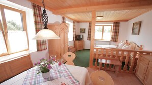 A cozy room with a wooden bed, a dining table with a plaid tablecloth, and a television on a wooden cabinet. - Pension Schweizerhaus (Weyarn)
