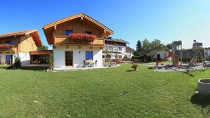 A hotel with multiple wooden buildings, a large grassy lawn, and a playground with a slide. - Pension Schweizerhaus (Weyarn)
