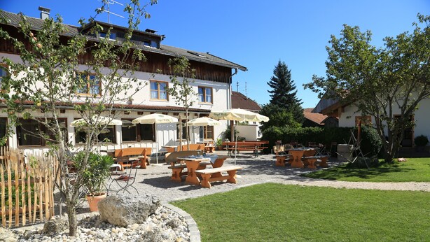 An outdoor seating area with tables and chairs, surrounded by a garden with a lawn and a rock border. - Pension Schweizerhaus (Weyarn)