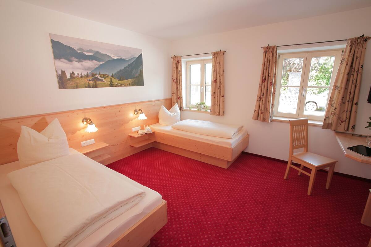 A room with two beds, a chair, a desk with a sink, and a window with curtains.