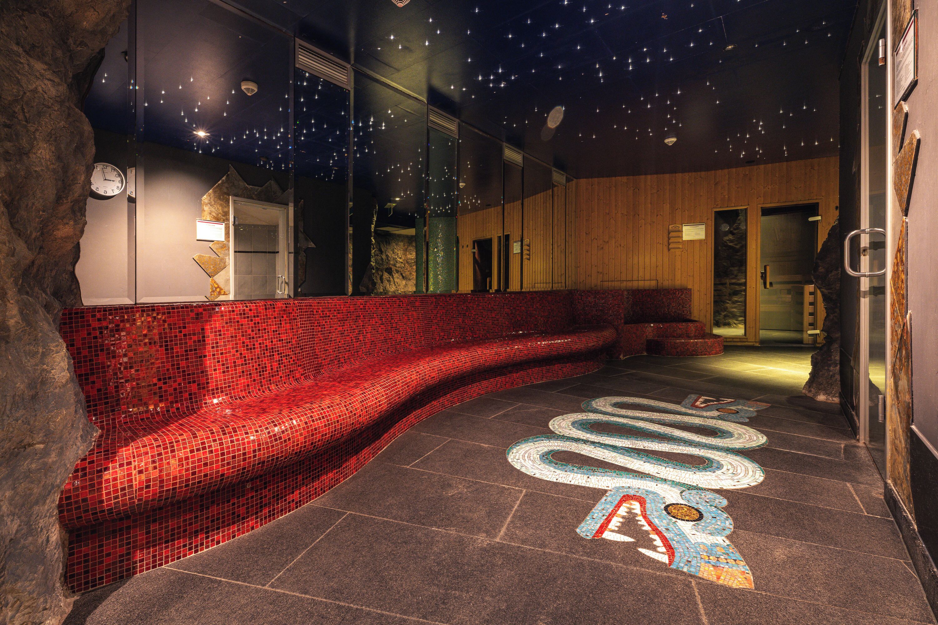 A modern spa area with a red mosaic bench, a starry ceiling, and a stone floor with a snake design.
