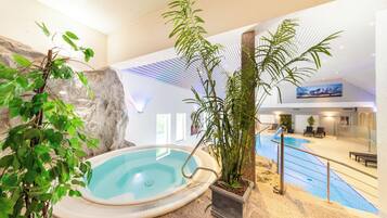 Una piscina interior con hidromasaje, rodeada de plantas y un muro de roca.
