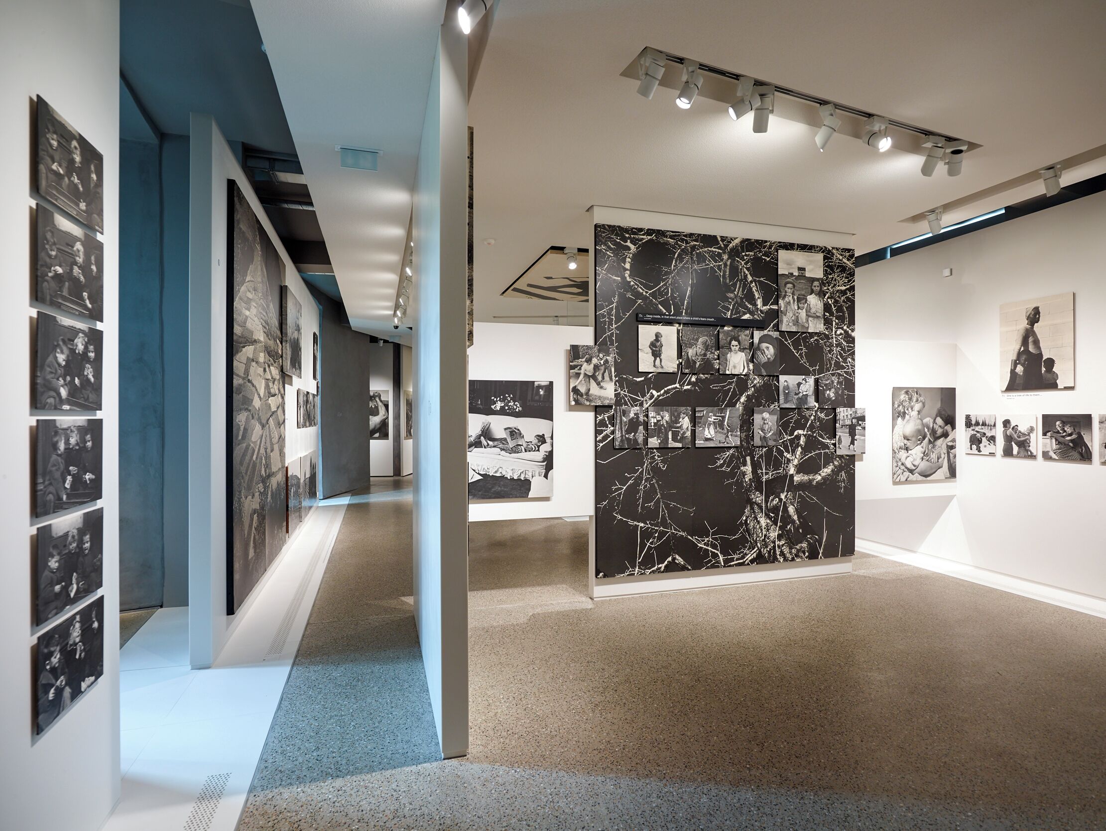 Uma galeria com fotografias a preto e branco nas paredes, uma parede de mármore com fotos e uma parede azul de destaque.