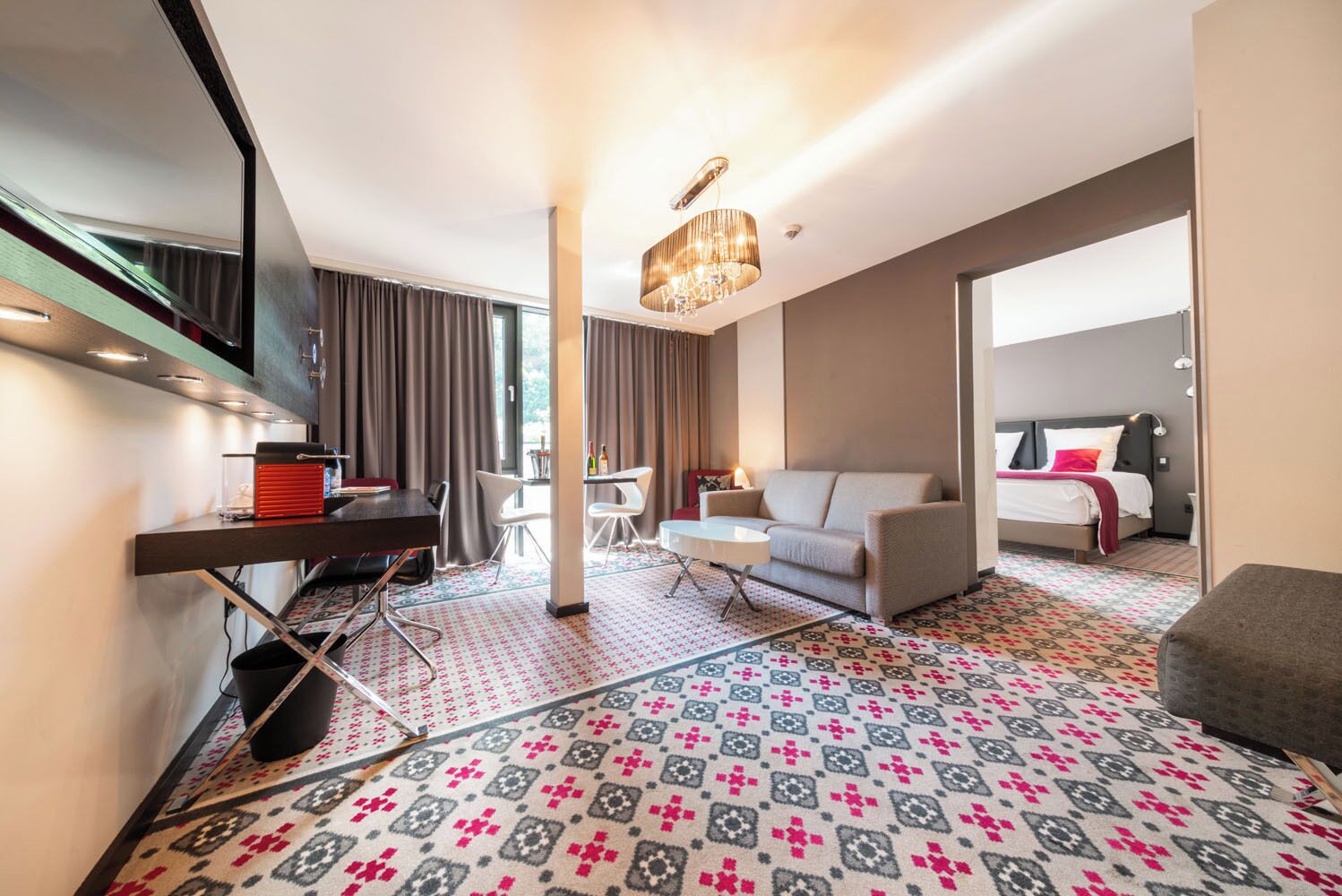 A modern hotel room with a large bed, a sofa, a desk, and a dining area.