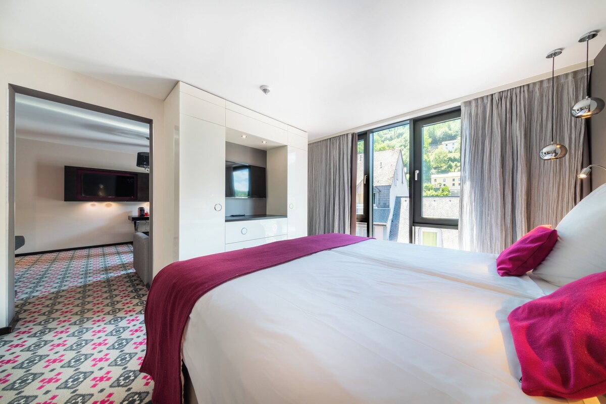 Una habitación de hotel moderna con una cama grande, un televisor montado en la pared y un balcón con cortinas.