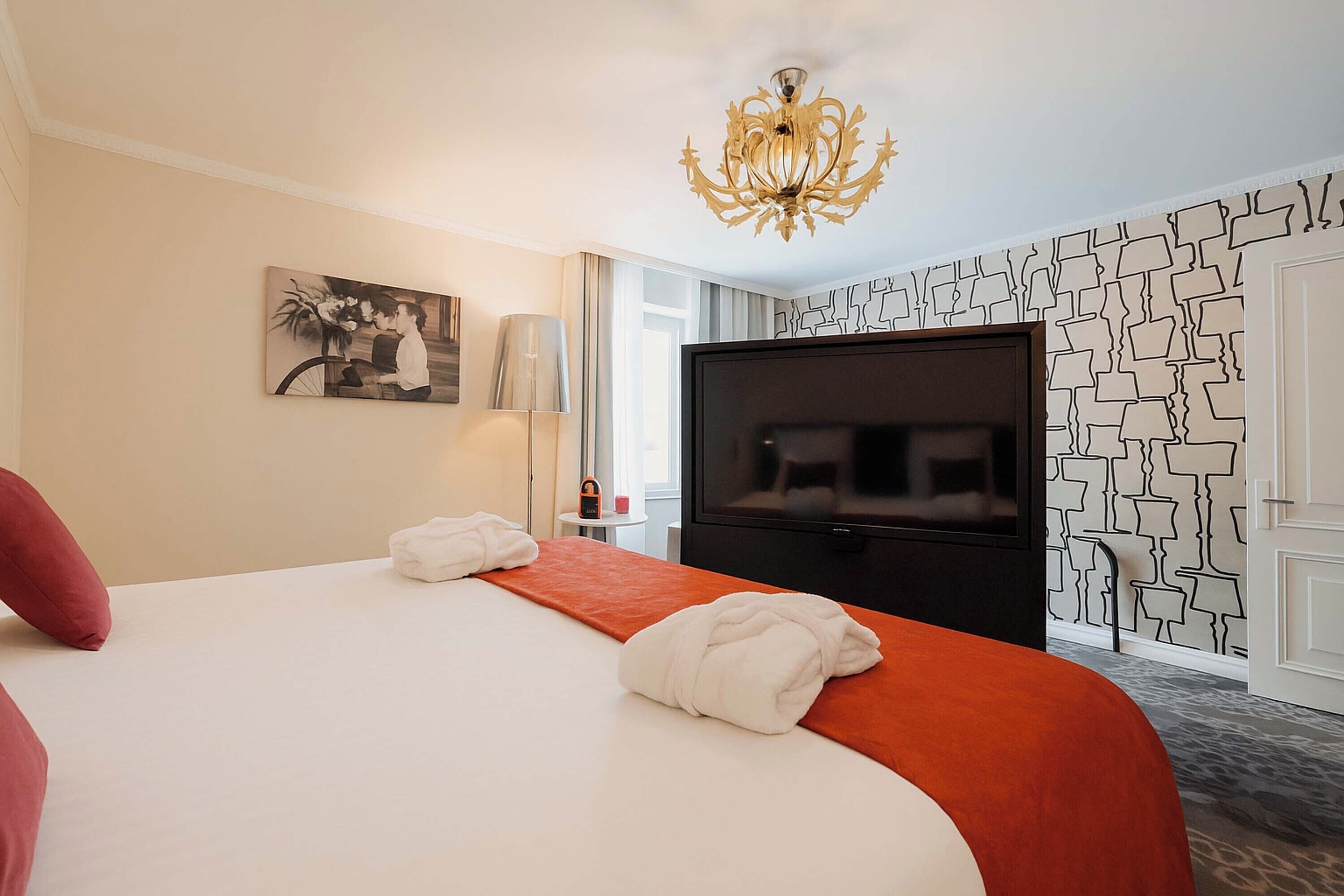 Una habitación de hotel con una cama grande, un televisor de pantalla plana, una araña y una pared con estampado.