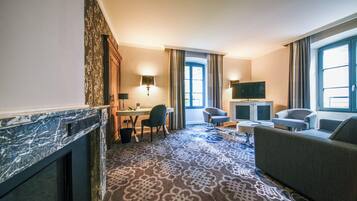A hotel room with a marble fireplace, a sofa, a TV, and a patterned carpet.