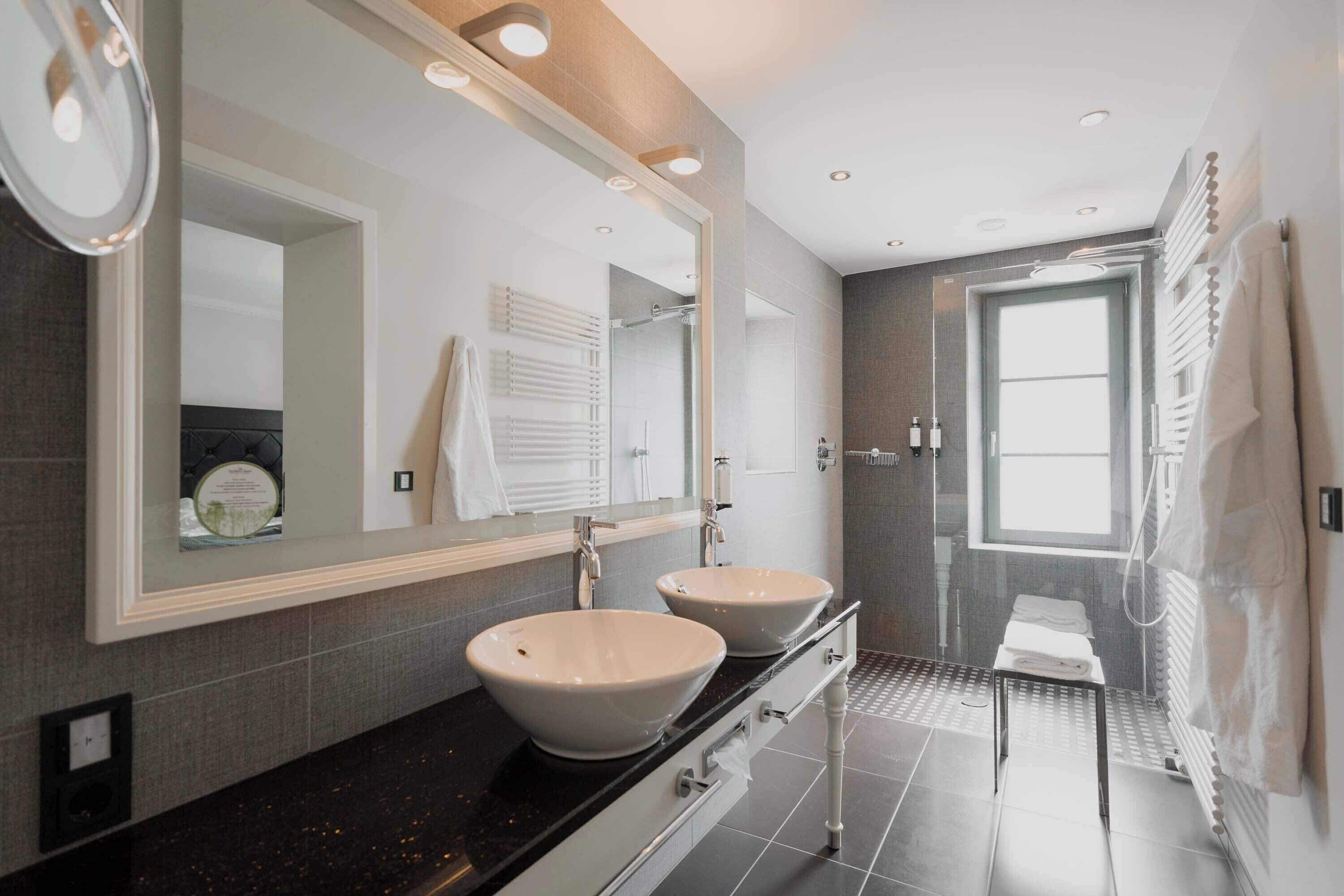 A modern bathroom with two sinks, a large mirror, and a walk-in shower.