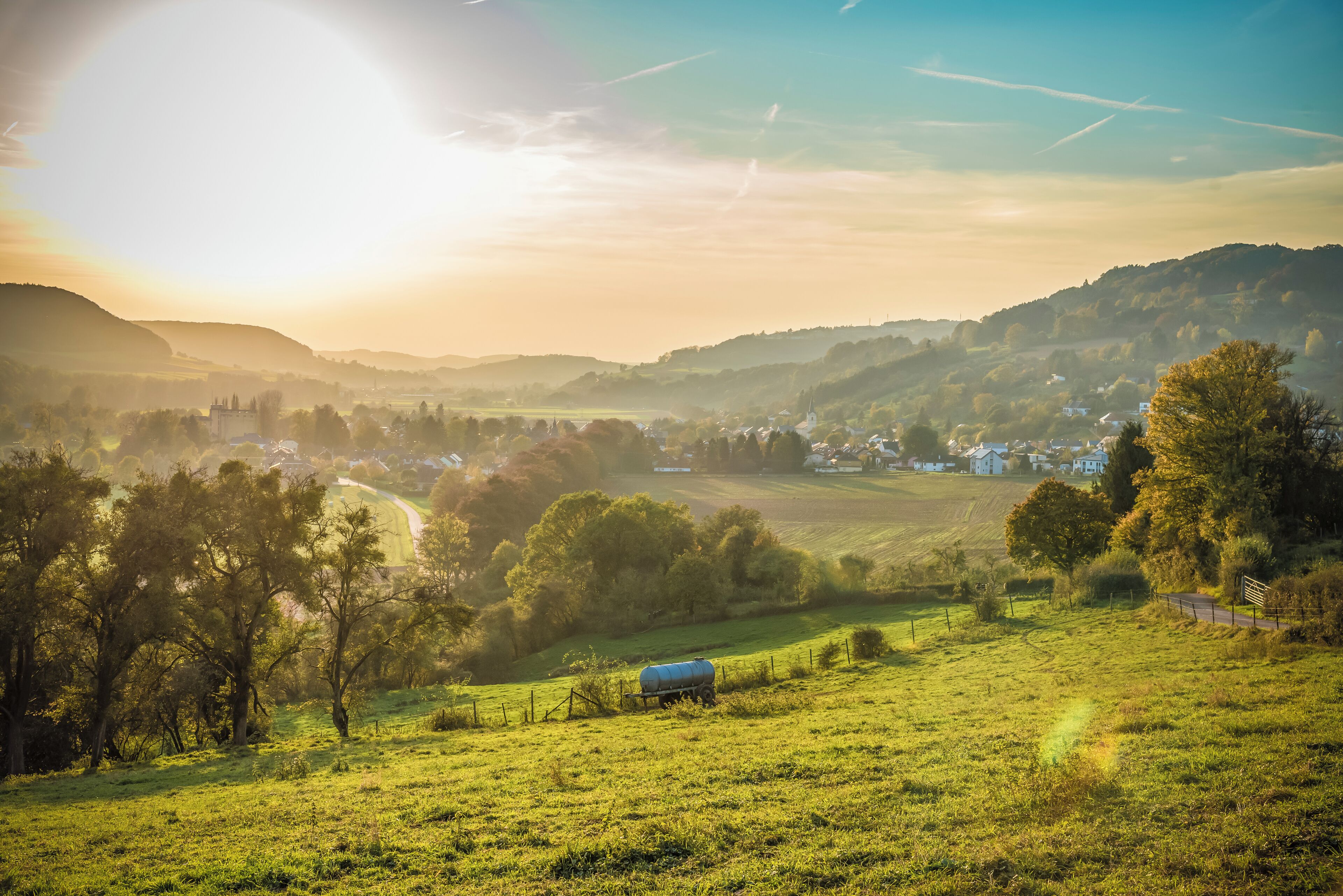 A rural landscape with rolling hills, a small blue water tank, and a few scattered houses.