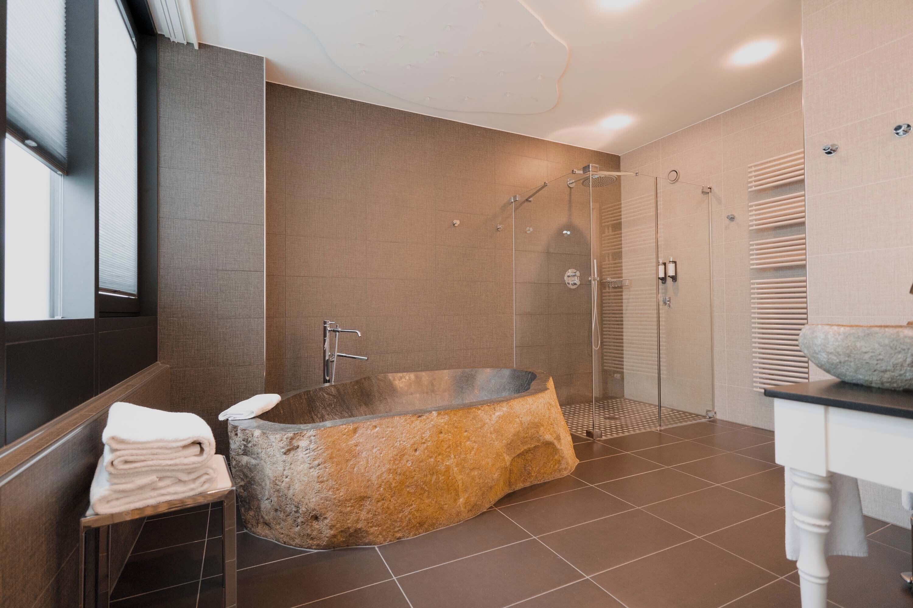 Un baño moderno con una bañera independiente, ducha con cerramiento de vidrio y tocador con lavabo de piedra.